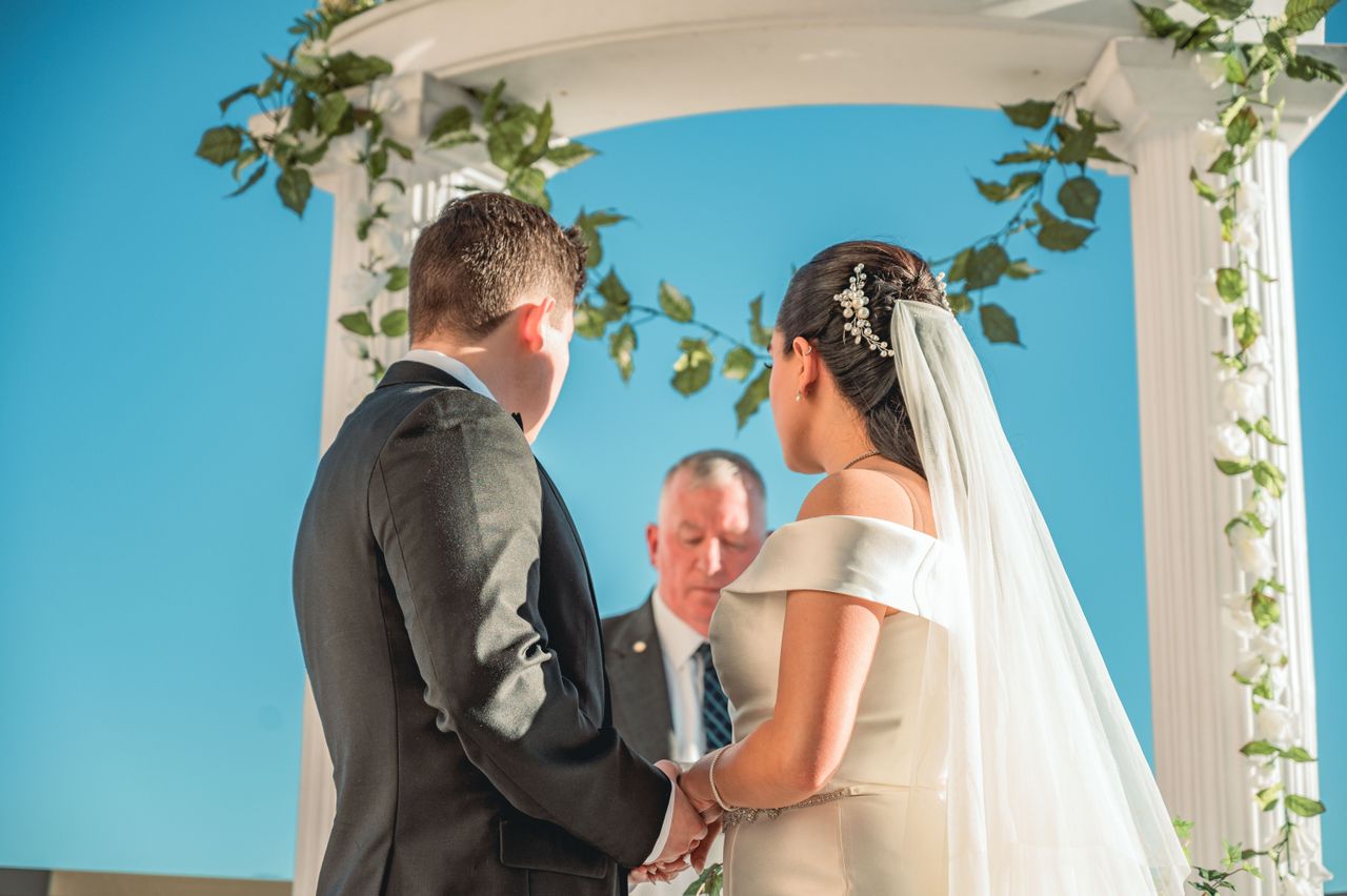 engagement-photography-03 Bride and groom holding hands in an outdoor ceremony under a floral arch.