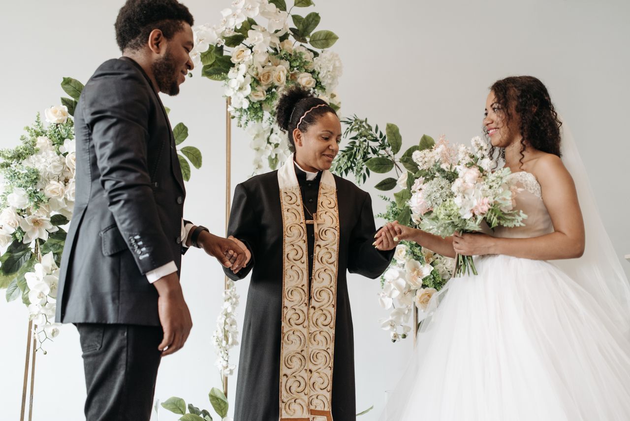 services-01 Elegant wedding ceremony showcasing a bride, groom, and pastor exchanging vows in a floral setting.